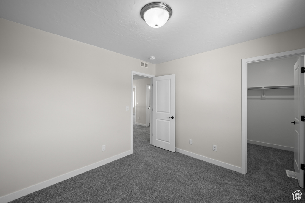 Unfurnished bedroom featuring dark colored carpet, a spacious closet, and a closet