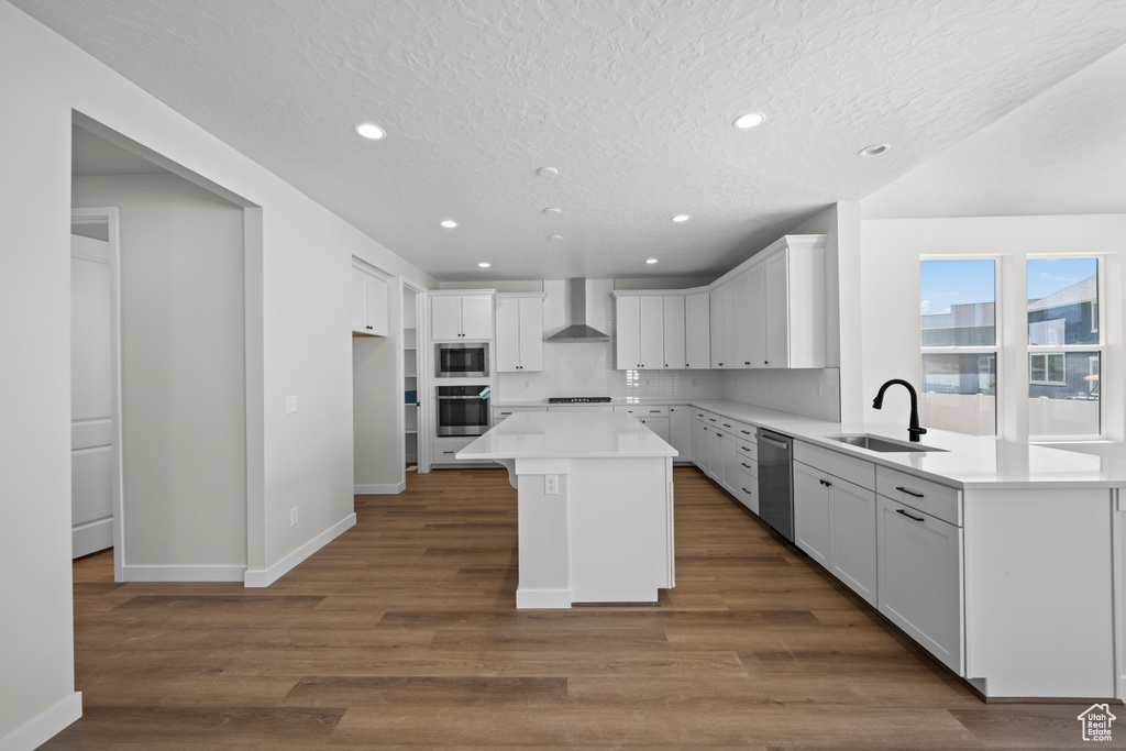 Kitchen featuring wall chimney range hood, a kitchen island, sink, dark hardwood / wood-style floors, and appliances with stainless steel finishes