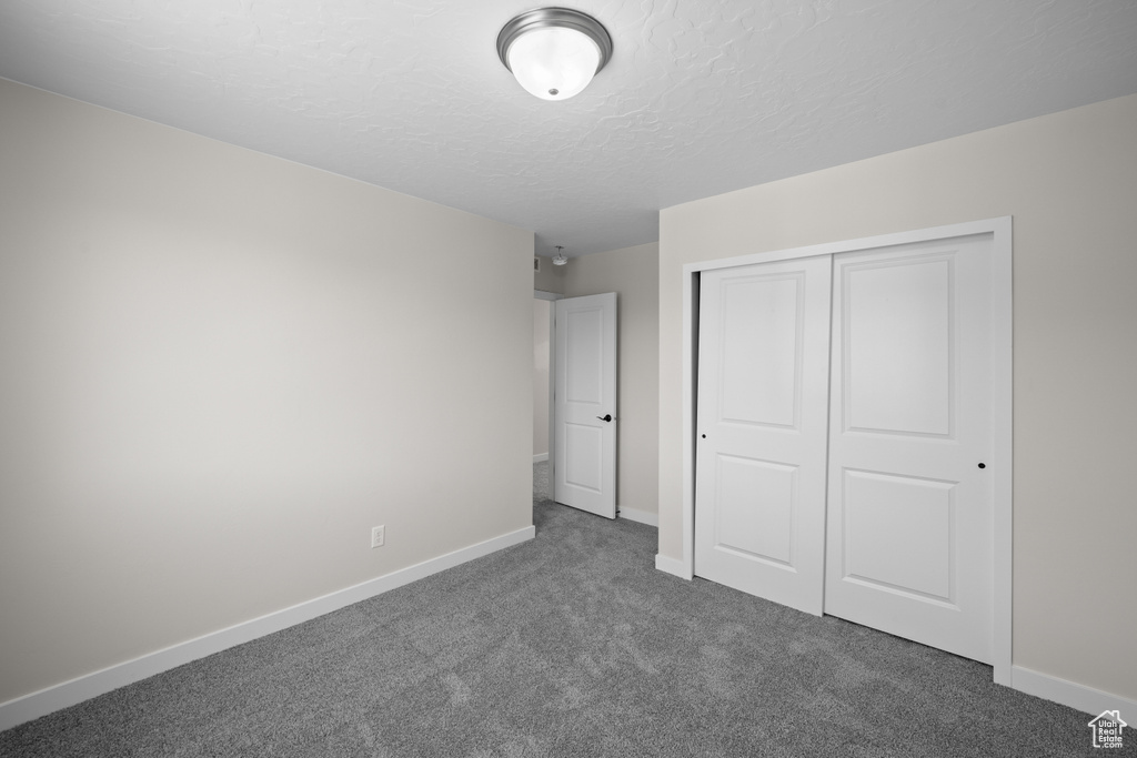 Unfurnished bedroom with a textured ceiling, a closet, and dark colored carpet