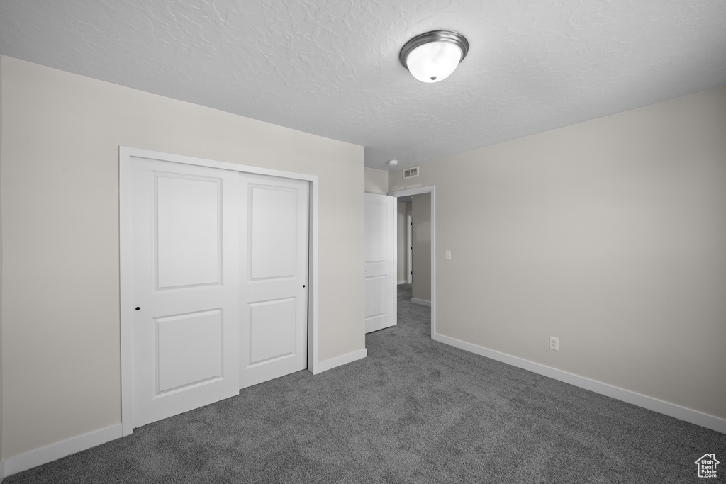 Unfurnished bedroom with a closet, dark carpet, and a textured ceiling