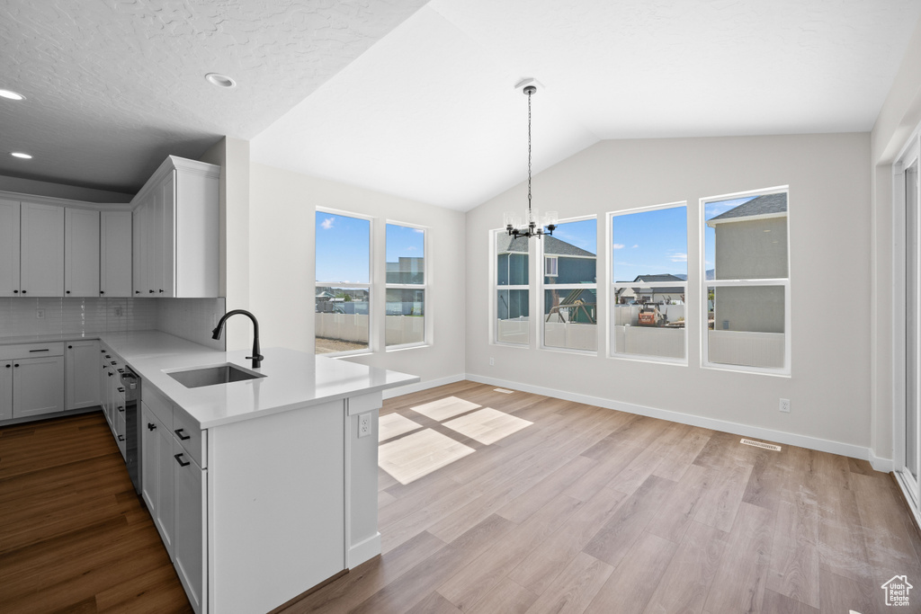 Kitchen with lofted ceiling, kitchen peninsula, sink, a notable chandelier, and light wood-type flooring