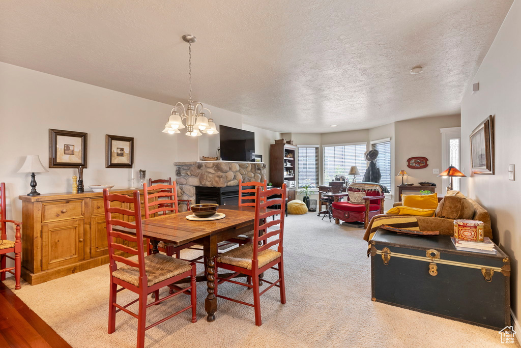 Carpeted dining area with a stone fireplace, a textured ceiling, and a notable chandelier