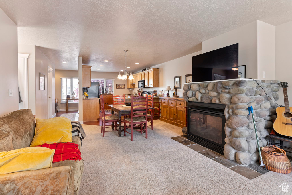 Living room with a notable chandelier, carpet, a textured ceiling, and a fireplace