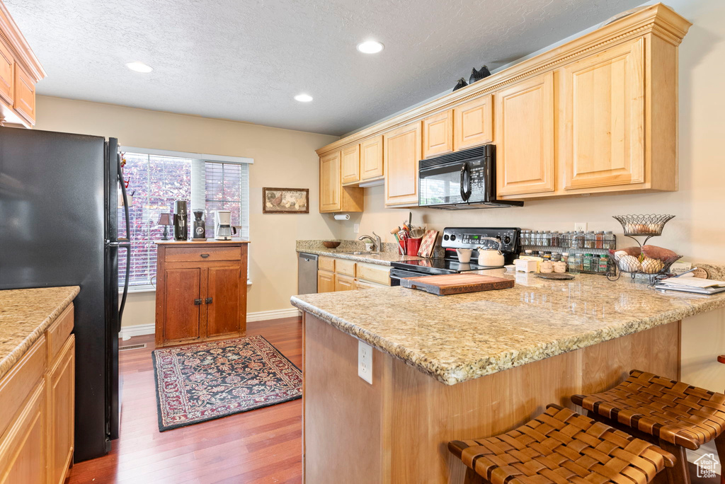 Kitchen featuring black appliances, a kitchen breakfast bar, light hardwood / wood-style floors, and kitchen peninsula