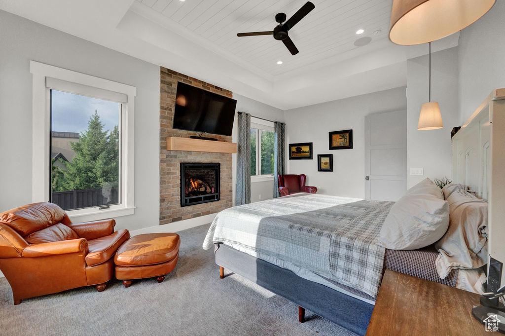 Carpeted bedroom with ceiling fan, a raised ceiling, and a fireplace