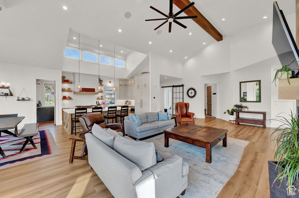 Living room with beamed ceiling, a towering ceiling, ceiling fan, and light wood-type flooring