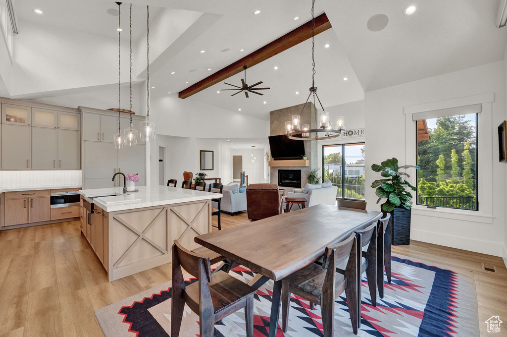 Dining area featuring light hardwood / wood-style floors, a fireplace, ceiling fan with notable chandelier, high vaulted ceiling, and beamed ceiling