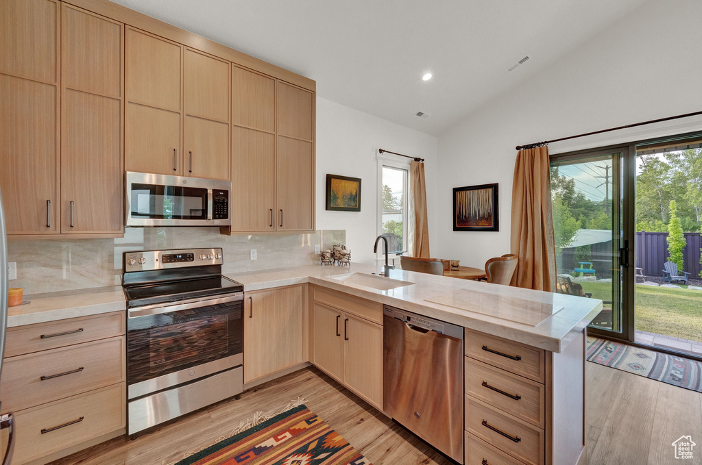 Kitchen with light hardwood / wood-style flooring, appliances with stainless steel finishes, tasteful backsplash, and kitchen peninsula