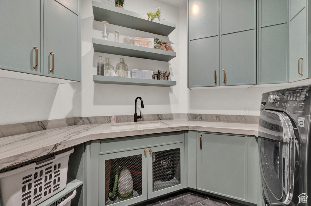 Clothes washing area featuring dark tile flooring, sink, washer / clothes dryer, and cabinets