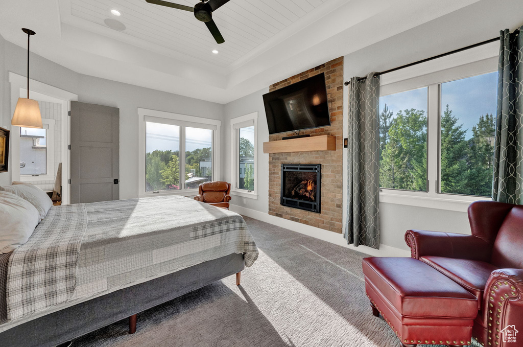 Carpeted bedroom featuring brick wall, a tray ceiling, a fireplace, and ceiling fan