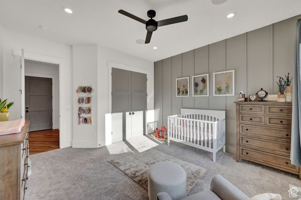 Carpeted bedroom featuring a nursery area and ceiling fan