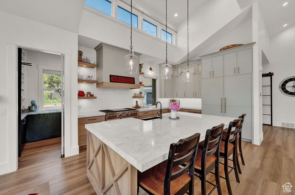 Kitchen featuring range with two ovens, a center island with sink, light hardwood / wood-style flooring, a high ceiling, and backsplash