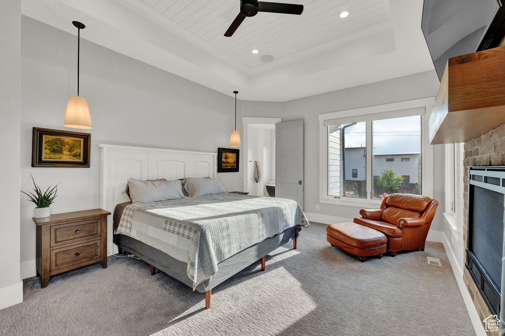 Bedroom with a stone fireplace, carpet floors, ceiling fan, and a raised ceiling