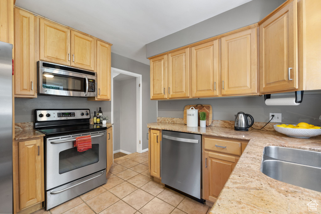 Kitchen with light brown cabinets, light tile flooring, light stone counters, and stainless steel appliances