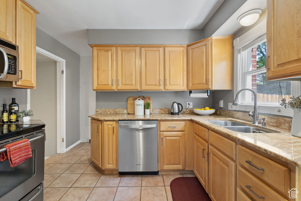 Kitchen with stainless steel appliances, light stone counters, sink, light tile flooring, and light brown cabinets