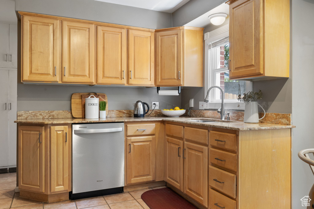 Kitchen with light stone counters, sink, light tile floors, and stainless steel dishwasher