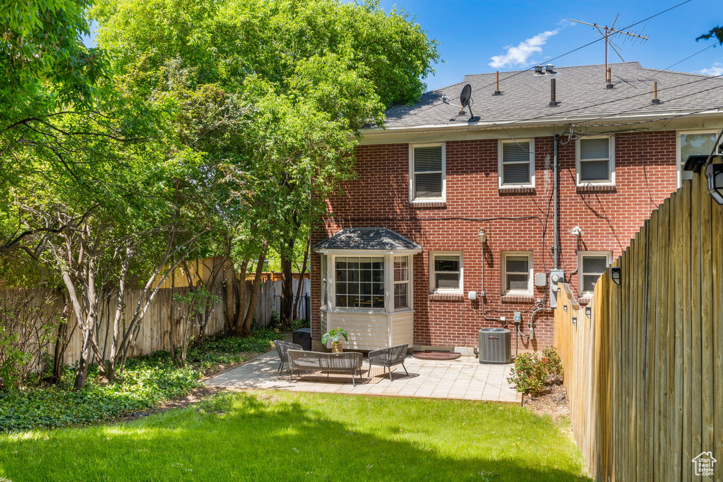 Rear view of house with a patio, central AC unit, and a lawn