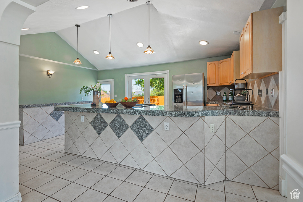 Kitchen with tasteful backsplash, stainless steel refrigerator with ice dispenser, pendant lighting, light tile floors, and lofted ceiling