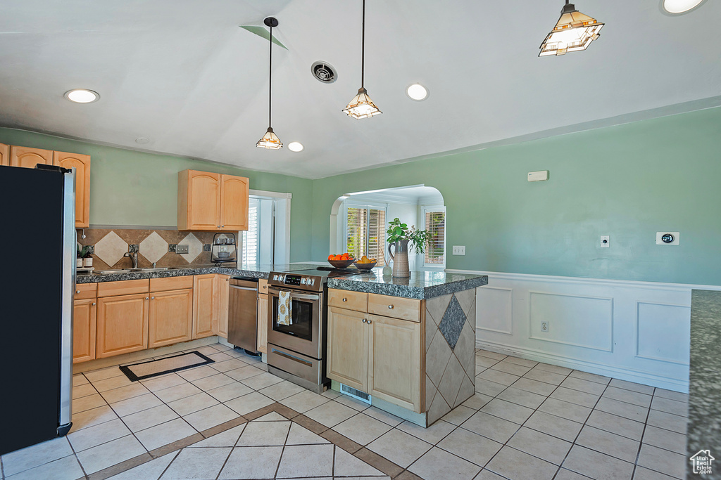 Kitchen featuring light brown cabinets, pendant lighting, backsplash, light tile floors, and appliances with stainless steel finishes