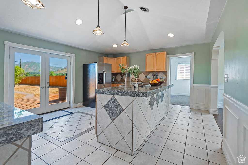 Kitchen with decorative light fixtures, stainless steel fridge with ice dispenser, backsplash, and light tile flooring