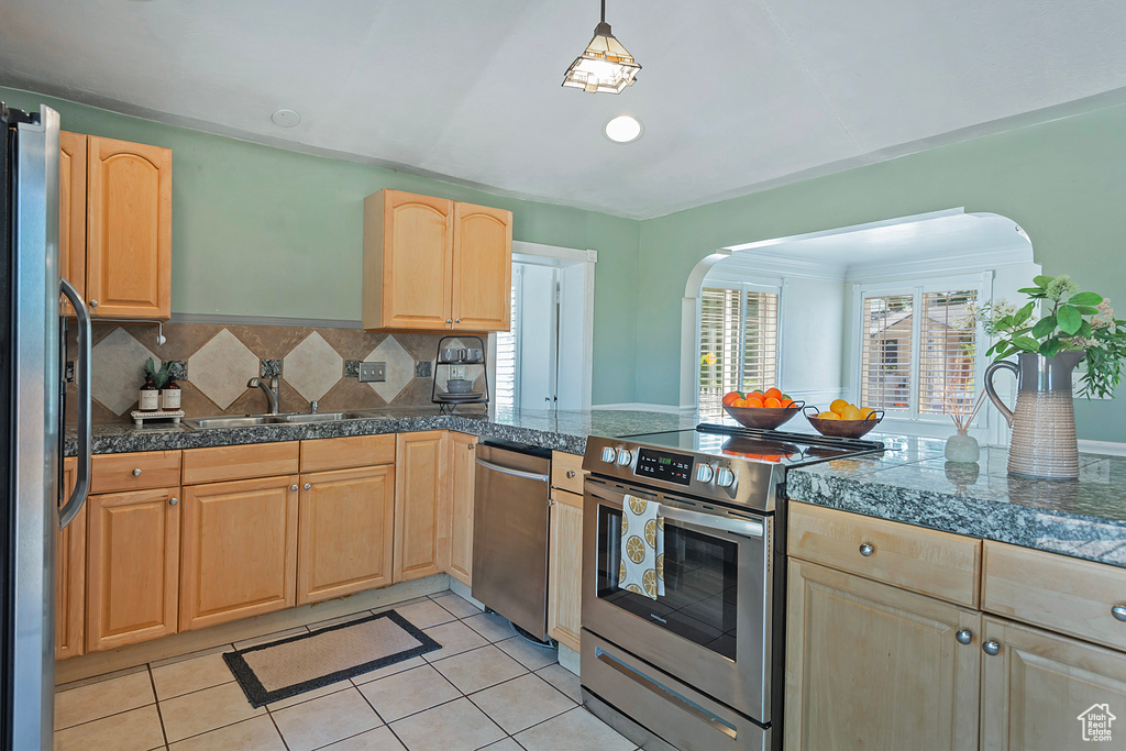 Kitchen with decorative light fixtures, backsplash, appliances with stainless steel finishes, sink, and light tile floors