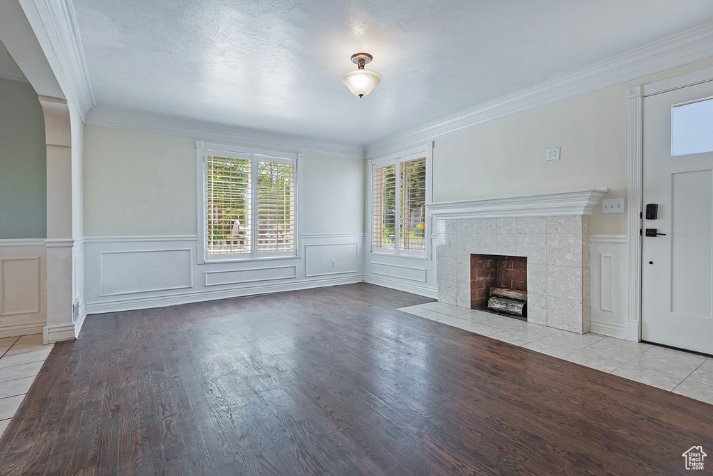 Unfurnished living room featuring hardwood / wood-style floors, a tiled fireplace, and crown molding