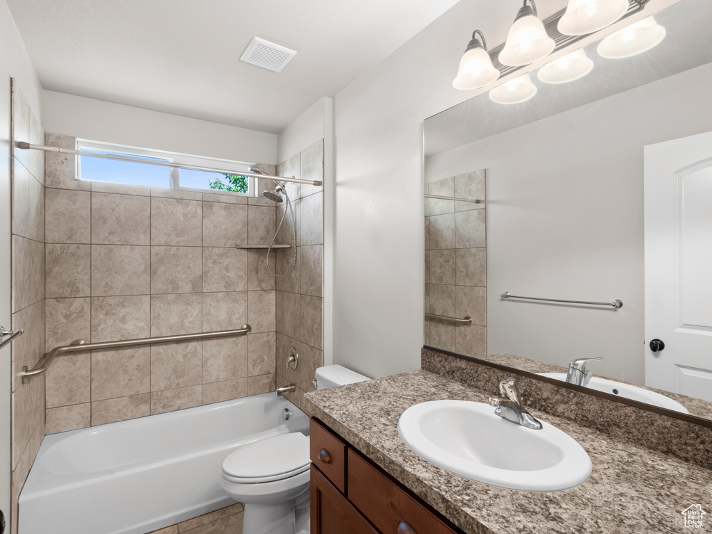 Full bathroom with tiled shower / bath, vanity with extensive cabinet space, tile flooring, and toilet