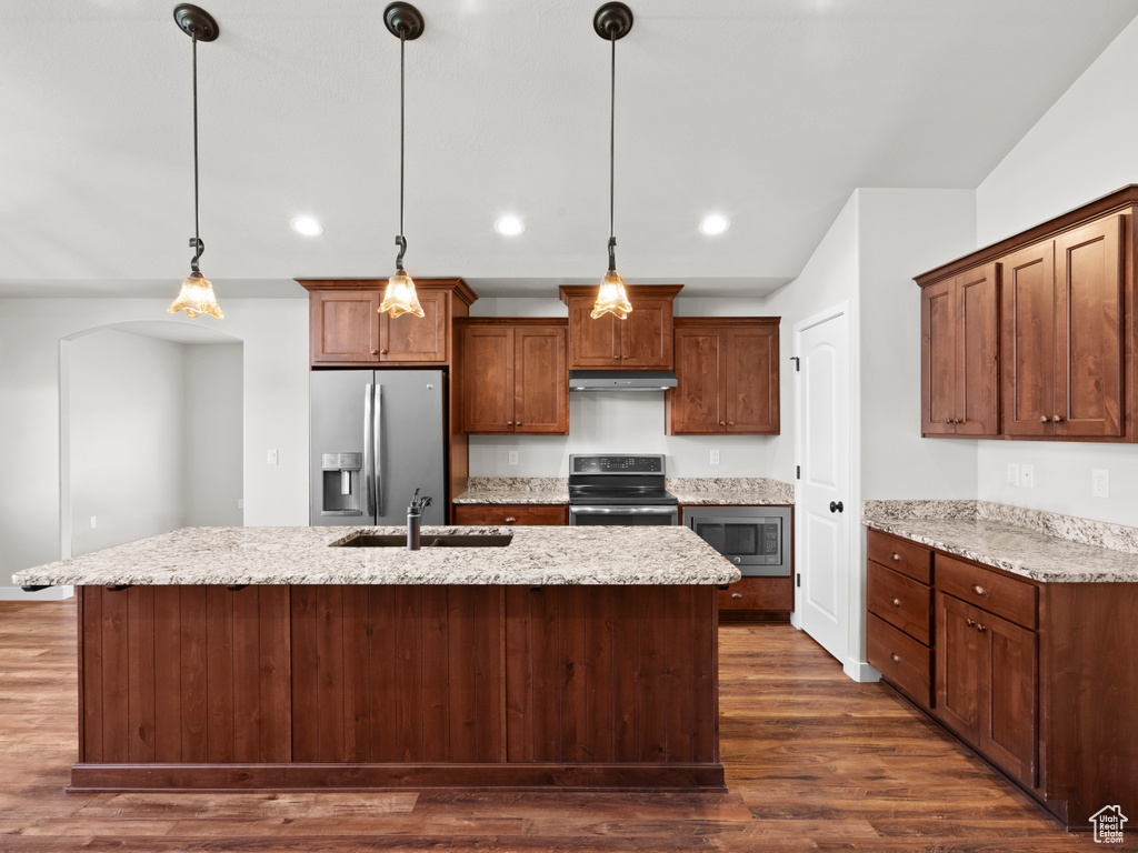 Kitchen featuring appliances with stainless steel finishes, decorative light fixtures, dark wood-type flooring, and an island with sink