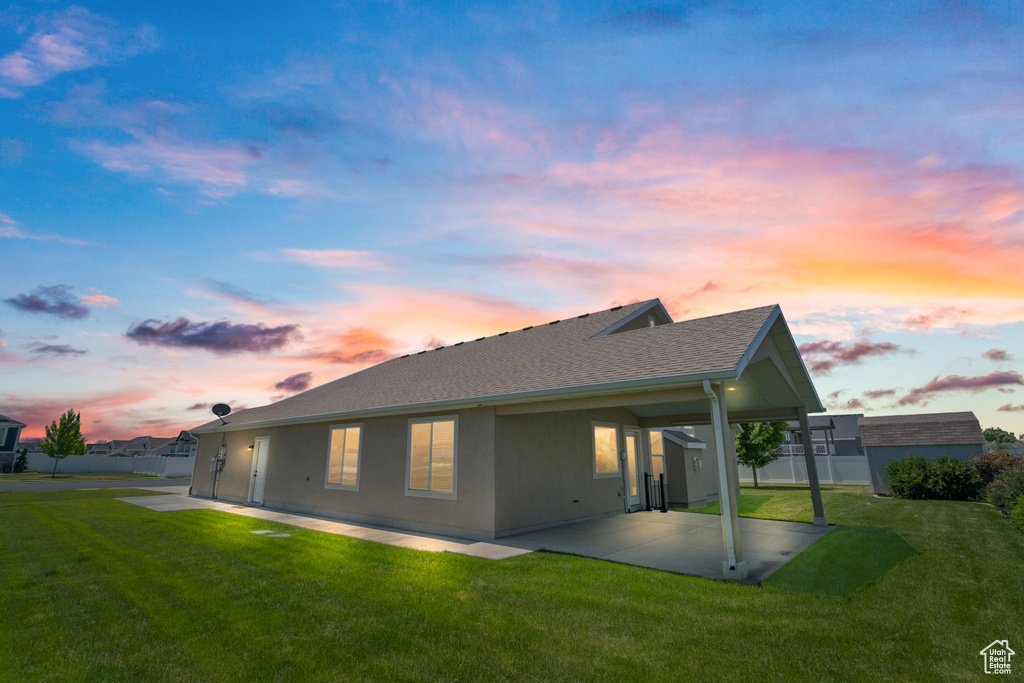 Back house at dusk with a patio area and a lawn