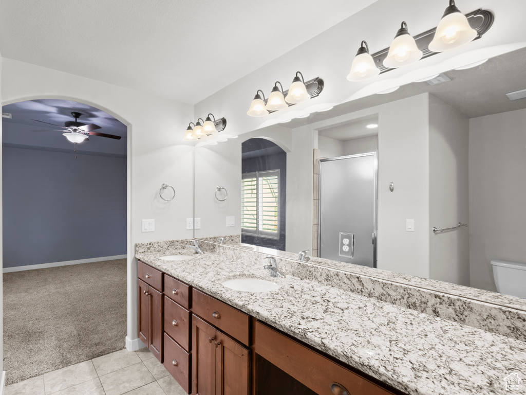 Bathroom featuring tile floors, large vanity, ceiling fan, toilet, and dual sinks