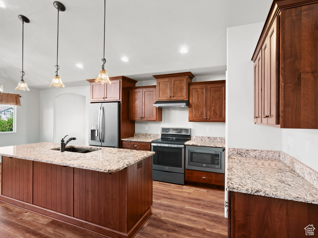 Kitchen with a center island with sink, pendant lighting, wood-type flooring, sink, and appliances with stainless steel finishes