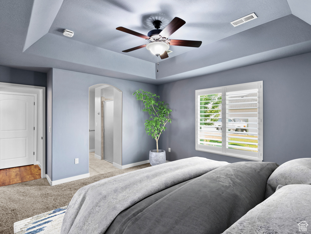 Bedroom featuring a tray ceiling, ceiling fan, connected bathroom, and light colored carpet