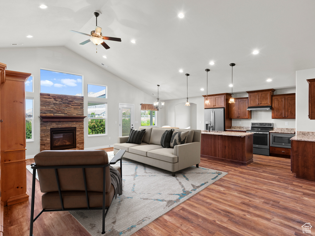 Living room with a stone fireplace, high vaulted ceiling, hardwood / wood-style flooring, and ceiling fan with notable chandelier