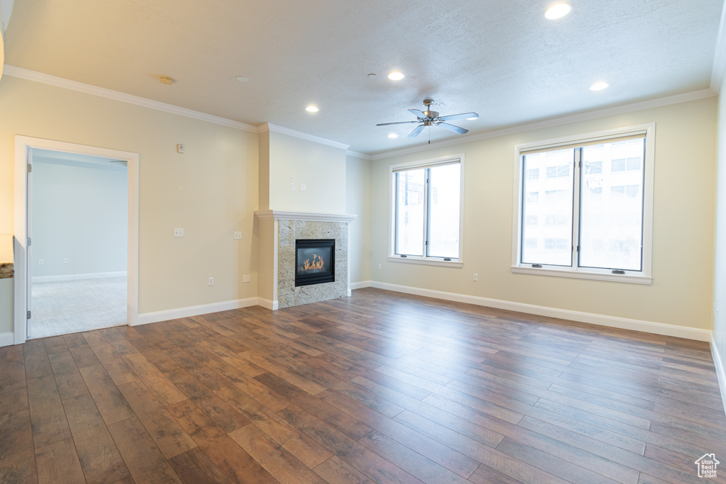 Unfurnished living room featuring dark hardwood / wood-style floors, ceiling fan, a tiled fireplace, and ornamental molding