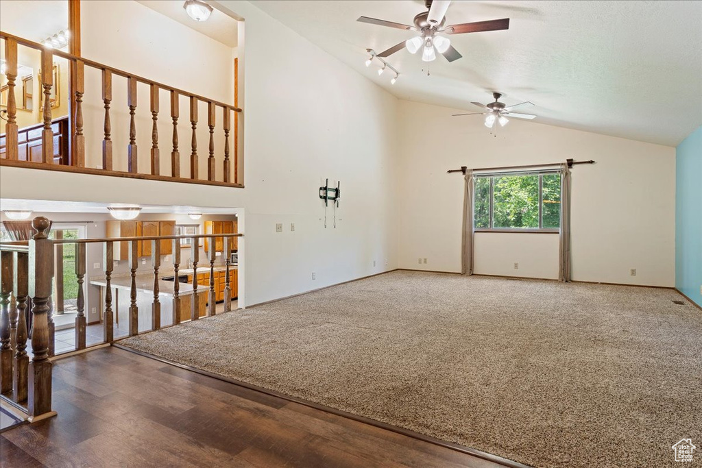 Unfurnished living room with high vaulted ceiling, ceiling fan, carpet floors, and track lighting