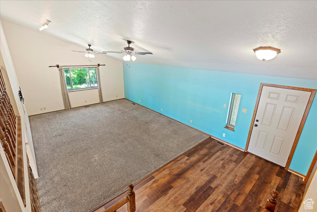 Foyer with ceiling fan, dark colored carpet, vaulted ceiling, and a textured ceiling