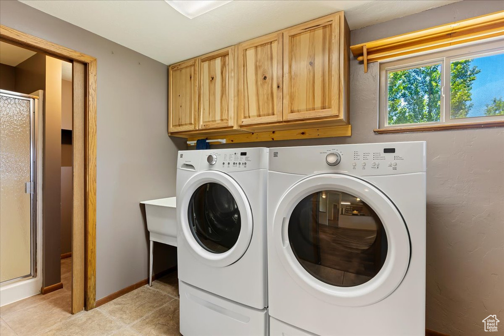 Laundry room with cabinets, washing machine and dryer, and light tile floors