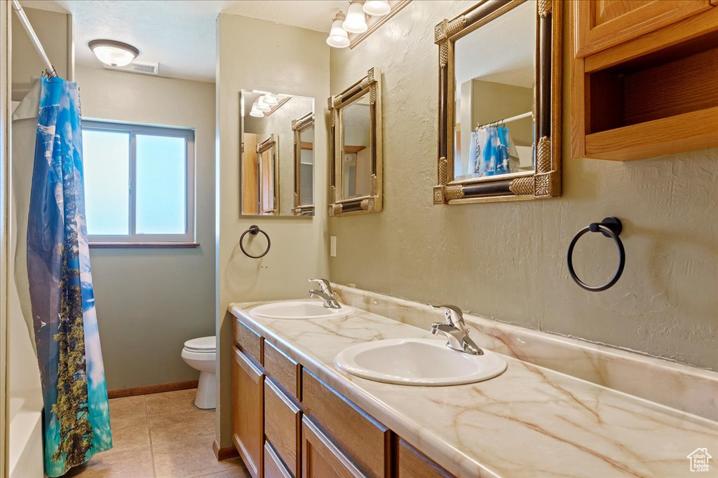 Full bathroom featuring double vanity, shower / bath combination with curtain, toilet, and tile floors