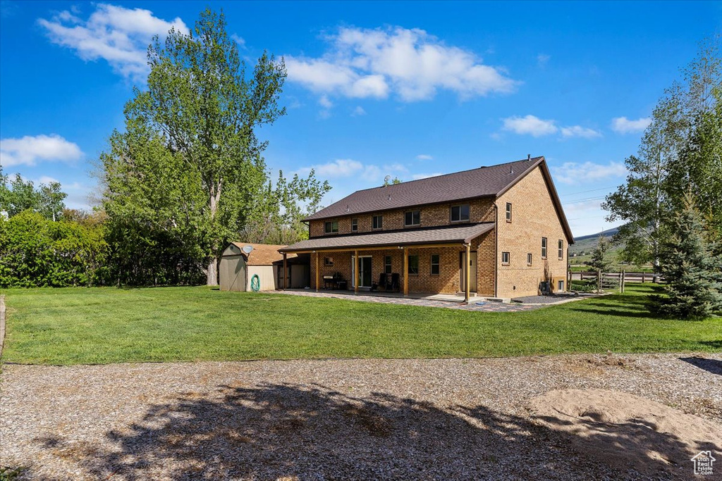 Back of property with a patio area, a lawn, and a storage shed