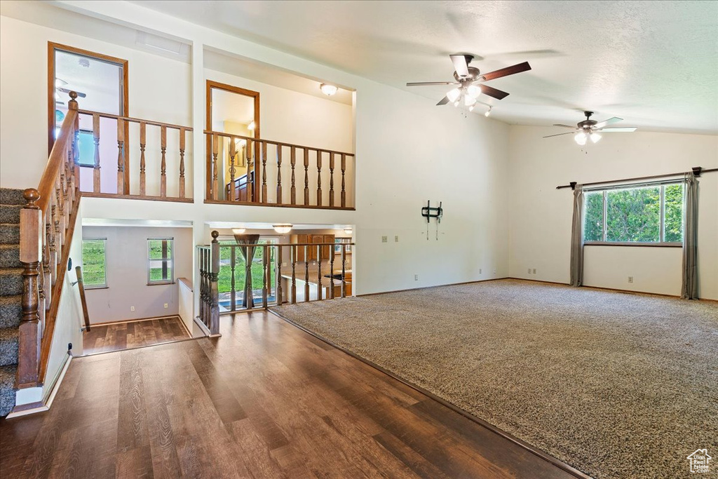 Unfurnished living room with high vaulted ceiling, a textured ceiling, ceiling fan, and dark carpet