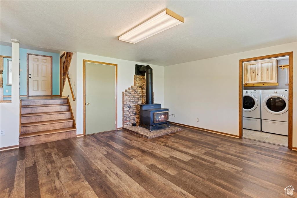 Unfurnished living room with washer and dryer, a textured ceiling, brick wall, hardwood / wood-style flooring, and a wood stove