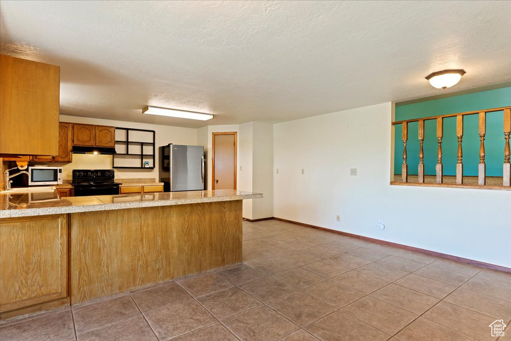 Kitchen with tile floors, stainless steel appliances, a textured ceiling, and kitchen peninsula