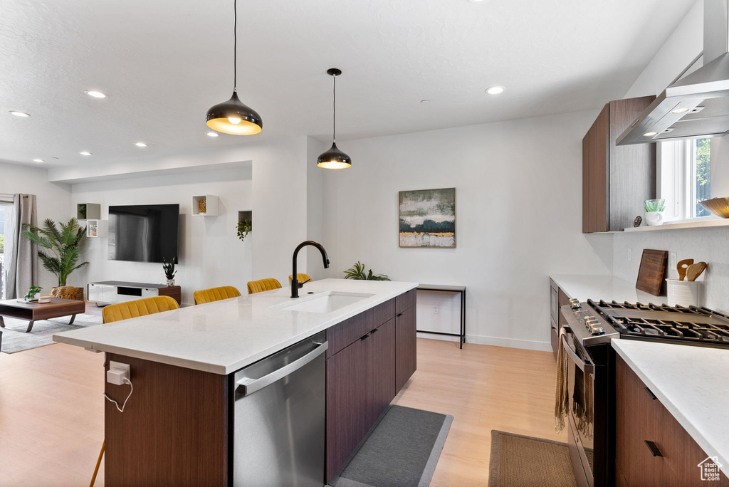 Kitchen with a center island with sink, decorative light fixtures, light wood-type flooring, sink, and appliances with stainless steel finishes