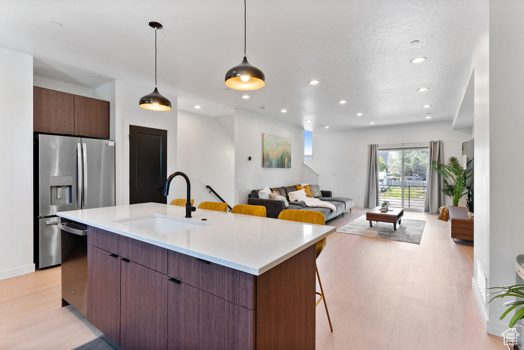 Kitchen featuring light stone counters, light hardwood / wood-style flooring, stainless steel appliances, a center island with sink, and sink