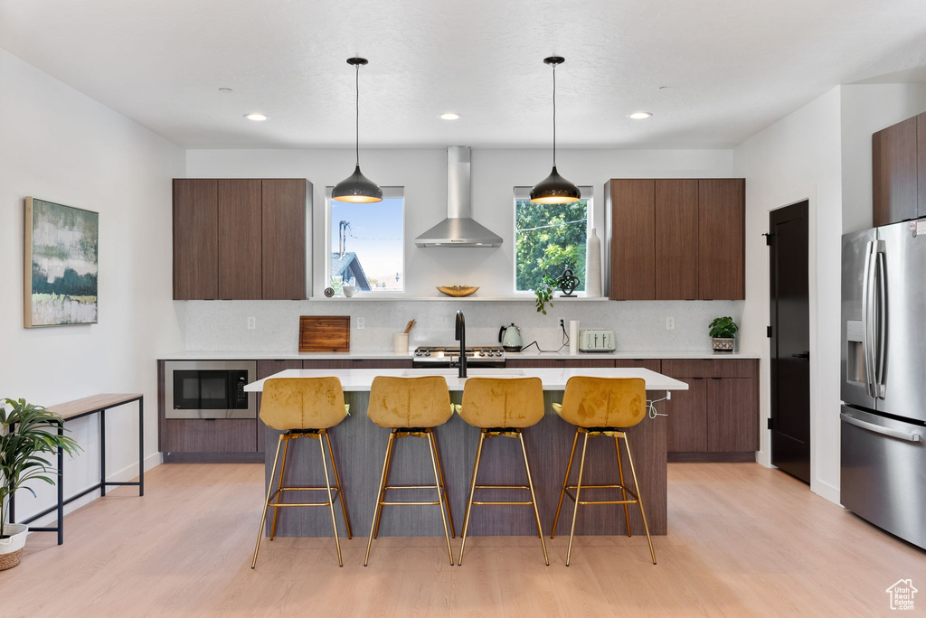 Kitchen featuring wall chimney range hood, stainless steel appliances, backsplash, and a kitchen island with sink