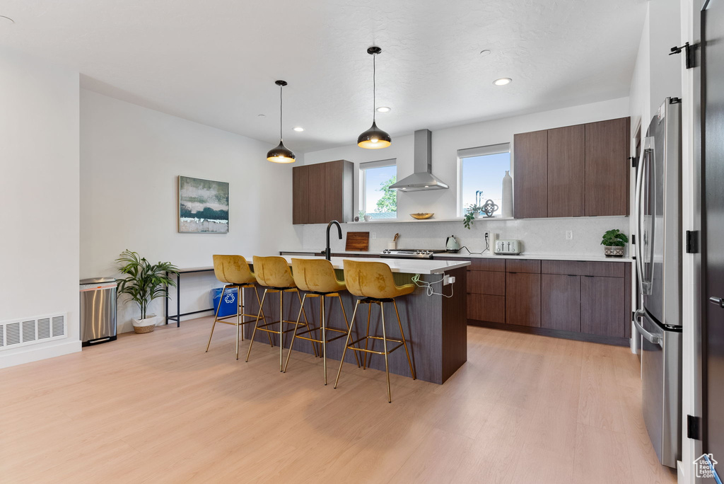 Kitchen with tasteful backsplash, a kitchen bar, wall chimney exhaust hood, dark brown cabinets, and light wood-type flooring