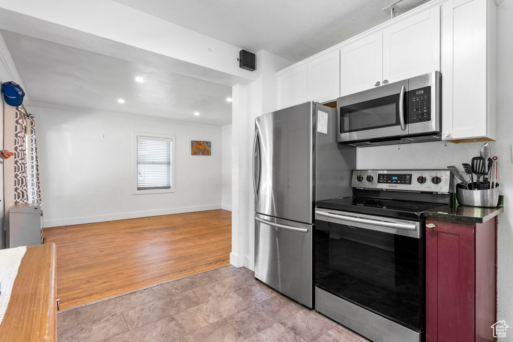 Kitchen featuring crown molding, stainless steel appliances, white cabinets, and light tile floors