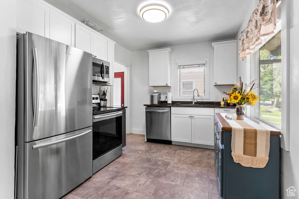 Kitchen featuring butcher block counters, stainless steel appliances, white cabinets, sink, and light tile flooring