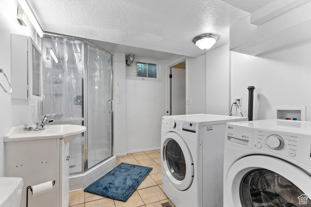 Clothes washing area with independent washer and dryer, a textured ceiling, light tile floors, and hookup for a washing machine