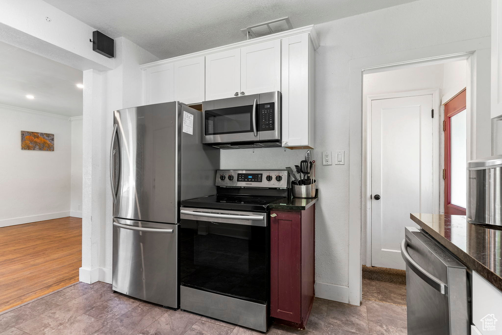 Kitchen with appliances with stainless steel finishes, white cabinetry, and hardwood / wood-style floors